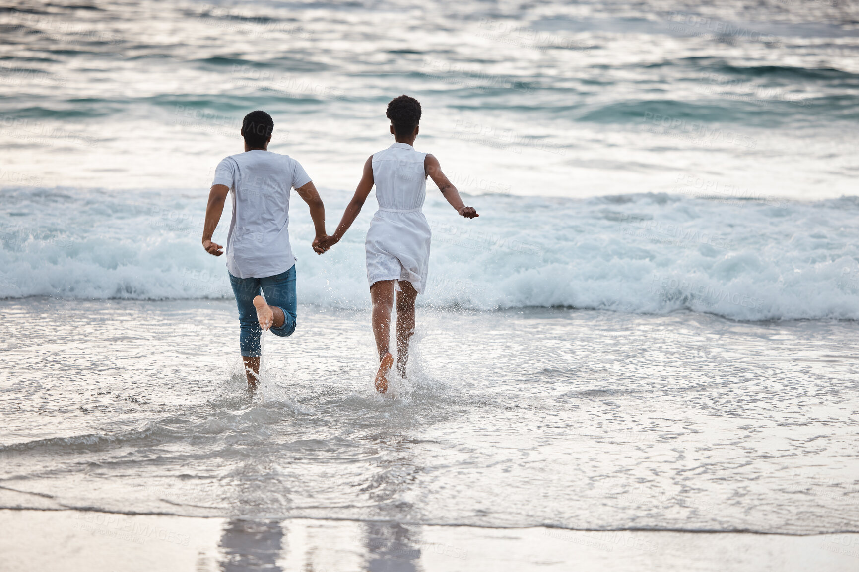 Buy stock photo Happy african American couple spending a day at the sea together. Cheerful boyfriend and girlfriend running into the water on the beach. Loving husband and wife bonding on the seashore