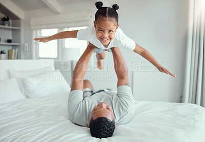 Buy stock photo Happy little mixed race girl lying in fathers arms while looking at the camera and smiling. Loving family with father lifting cute little child daughter playing plane and having fun on bed