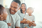 Happy funny mixed race family with two children wearing pyjamas and sitting together at home. Cheerful father laughing and playing with his son while having fun at home
