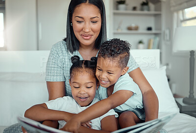 Buy stock photo Young mixed race mother reading a storybook while relaxing at home with her two children. Smiling parent telling small kids funny fairy tale story kids pointing at book while they sit together