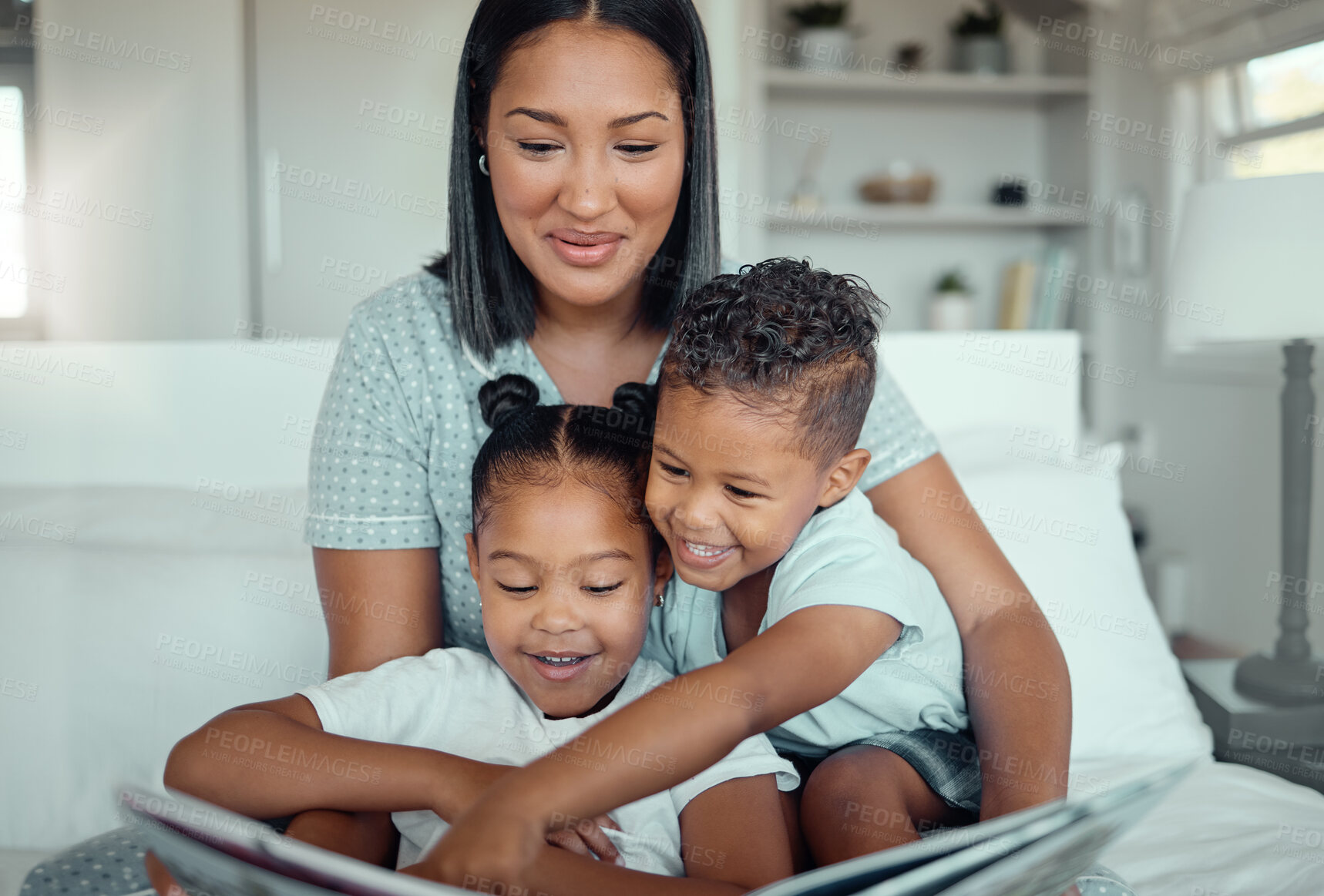 Buy stock photo Young mixed race mother reading a storybook while relaxing at home with her two children. Smiling parent telling small kids funny fairy tale story kids pointing at book while they sit together