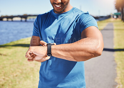Fit hispanic athlete checking his smartwatch to track his progress while running outside. Athletic man checking the time on his watch while jogging by a river. Smiling man exercising outside.