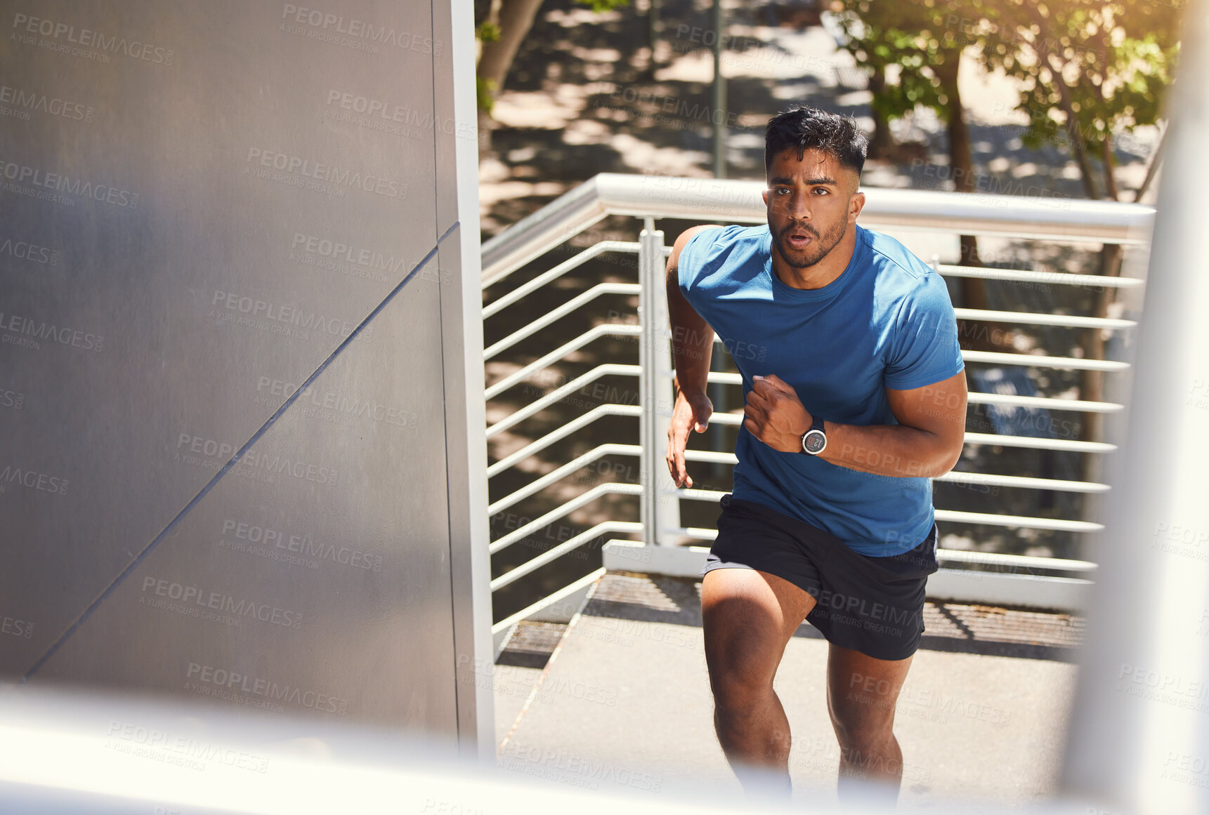 Buy stock photo Handsome mixed race athletic man running up the steps on of a building while focused on his fitness. Hispanic male serious about his health while doing cardio and working on his speed and energy.