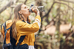 One young female only active caucasian woman drinking water out of a plastic bottle while hiking and wearing a backpack in the forest. Young brunette woman quenching her thirst because she feels dehydrated on her walk in the outdoors