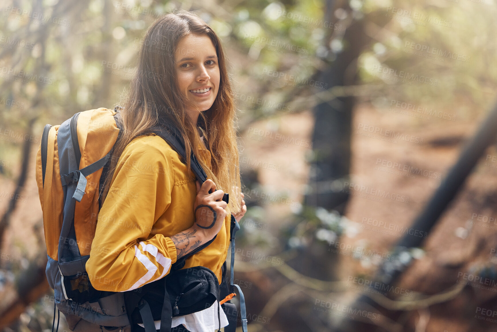 Buy stock photo One young active caucasian woman wearing a backpack while out hiking in the forest. Young brunette female walking alone in the woods. She loves being outdoors in nature. Hiking is her favourite hobby