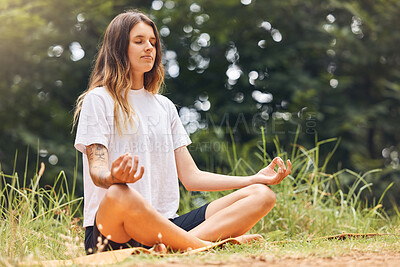 Buy stock photo A calm young caucasian female sitting with her legs crossed doing yoga and meditating on grass in a park on a sunny day. Young woman focusing her zen and energy while working on her mental wellness and relaxing in a forest 



