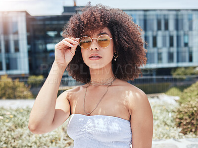 Portrait of young trendy beautiful mixed race woman with an afro smiling and posing alone outside. Hispanic woman wearing sunglasses and feeling happy. Fashionable african american woman in the city