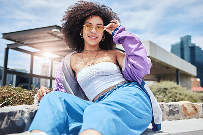 Portrait of young trendy beautiful mixed race woman with an afro smiling and posing alone outside. Hispanic woman wearing sunglasses and feeling happy. Fashionable African American woman in the city