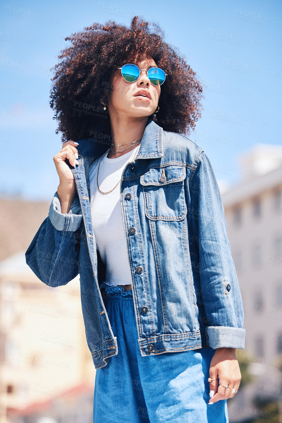 Buy stock photo Cool and fashionable hispanic woman wearing sunglasses outside. Cheerful young mixed race woman with a curly afro wearing a trendy, stylish denim jacket while enjoying a summer day at the park outside