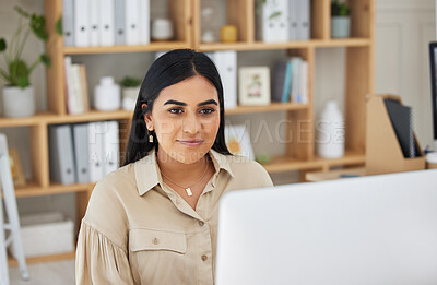 One beautiful young mixed race business woman working on her computer in the office at work. Confident and successful female entrepreneur of indian ethnicity working on a desktop in her workplace.