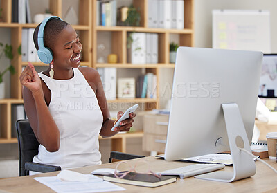 Young happy african american woman sitting at her desk at work and listening to music with her wireless headphones and smartphone while dancing to the rhythm. Black business woman taking a break,having fun relaxing and enjoying her break at her job