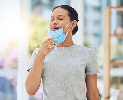 Young mixed race woman taking off her covid face mask and breathing fresh air inside a room. Hispanic enjoying clean oxygen after wearing disposable mask. Healthy and protected from virus pandemic