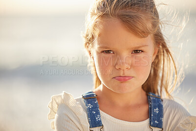 Buy stock photo Portrait view of a little young brunette caucasian girl having an upset and unhappy expression on her face while standing outside on the beach on a sunny summer day. Cheeky little female looking grumpy,, insulted, irritated, and displeased 

