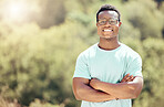 One handsome young african american male wearing glasses and standing outside with his arms folded. Happy and confident black man smiling while spending the day outdoors in nature. I love summer