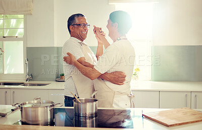 Buy stock photo A loving senior mixed race couple wearing aprons having fun standing and dancing in the kitchen at home. Romantic mature husband and wife smiling and laughing while doing the waltz in the kitchen inside their house  