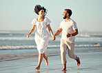 Happy mixed race young couple holding hands while walking on the beach together. Hispanic couple traveling and enjoying vacation and being romantic on the beach