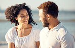 Happy mixed race young couple holding hands while walking on the beach together. Hispanic couple traveling and enjoying vacation and being romantic on the beach
