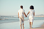 Rear view of mixed race young couple holding hands while walking on the beach together. Hispanic couple traveling and enjoying vacation and being romantic on the beach