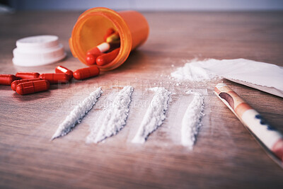 Lines of cocaine, an open bottle of pills and paper money bent into a roll on a wooden table. Cocaine is a highly addictive stimulant narcotic. It is used as a recreational drug to get high and party