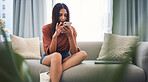 Attractive young mixed race woman sitting on the couch and using her smartphone to browse the internet, using mobile app or messaging on social network at home