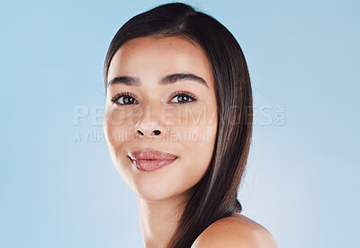 Portrait of one beautiful young hispanic woman with healthy skin and sleek hair posing against a blue studio background. Mixed race model with flawless complexion and natural beauty