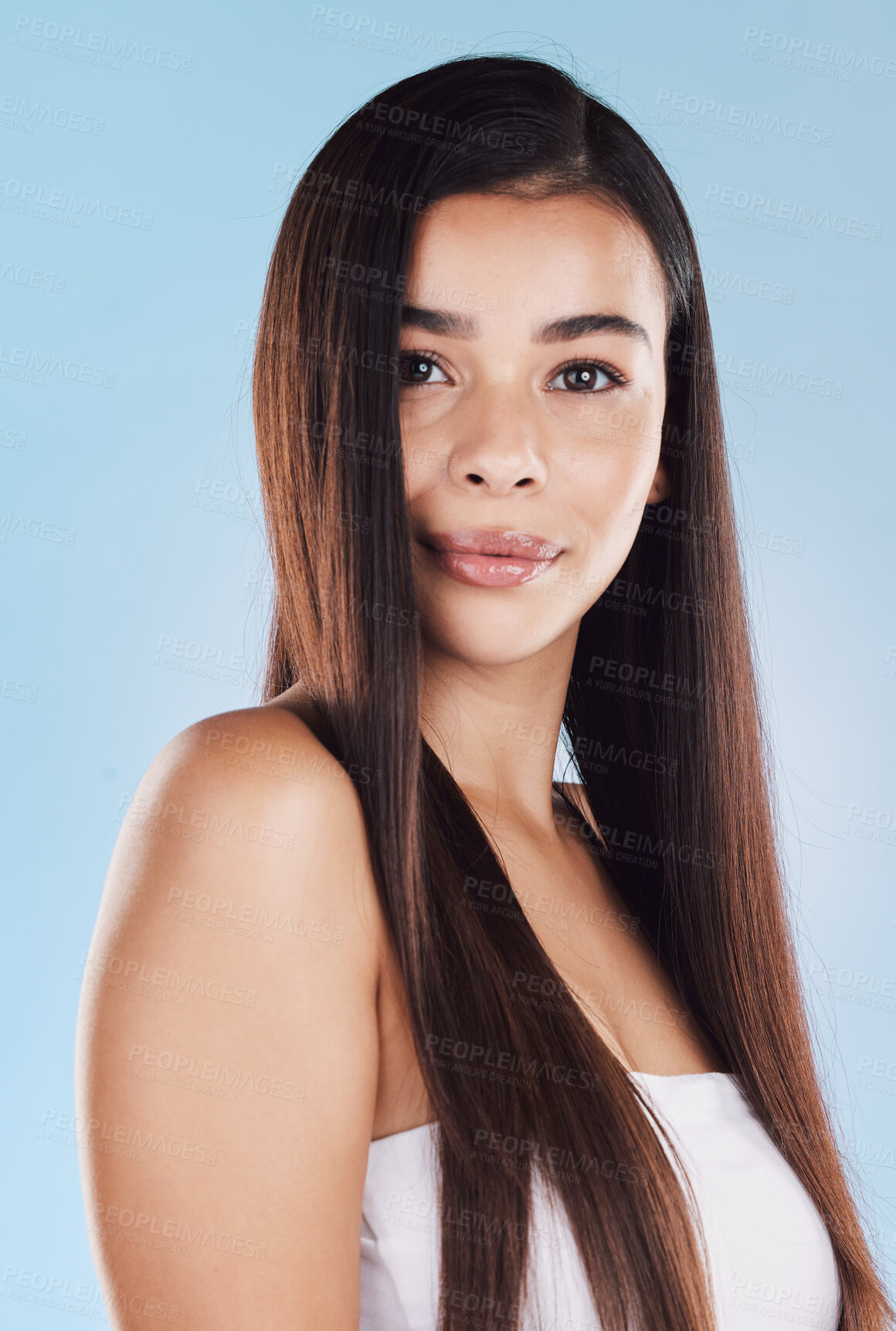 Buy stock photo Portrait of one beautiful young hispanic woman with healthy skin and sleek long hair posing against a blue studio background. Mixed race model with flawless complexion and natural beauty
