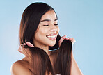 One beautiful young hispanic woman touching her sleek, silky and healthy long hair while smiling against a blue studio background. Confident and happy mixed race model with flawless complexion and natural beauty