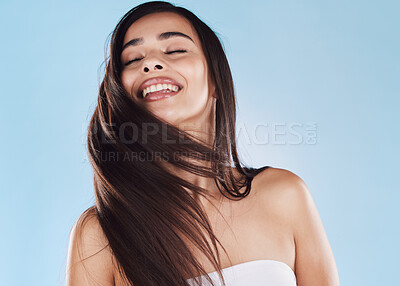 One beautiful young hispanic woman with healthy skin tossing her sleek long hair against a blue studio background. Happy mixed race model with flawless complexion and natural beauty