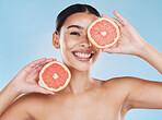 Beautiful young mixed race woman with a grapefruit isolated in studio against a blue background. Her skincare regime keeps her fresh. For glowing skin, eat healthy. Packed with vitamins and nutrients