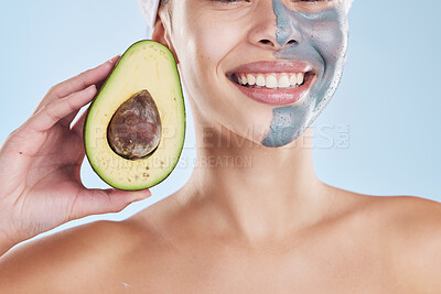 Beautiful young mixed race woman wearing a face mask peel and posing with an avocado isolated in studio against a blue background. A skincare regime keeps her fresh. Packed with vitamins and nutrients