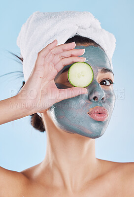 Beautiful young mixed race woman wearing a face mask peel and towel while holding cucumber slices. Attractive female clean and fresh out the shower and applying her daily skincare regime to her face