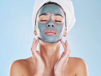 Beautiful young mixed race woman applying a face mask peel isolated in studio against a blue background. Attractive woman with a towel on her head after a shower. Her skincare regime keeps her fresh