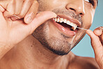 Closeup of one mixed race man flossing his teeth against a blue studio background. Guy grooming and cleaning his mouth for better oral and dental hygiene. Floss daily to prevent tooth decay and gum disease