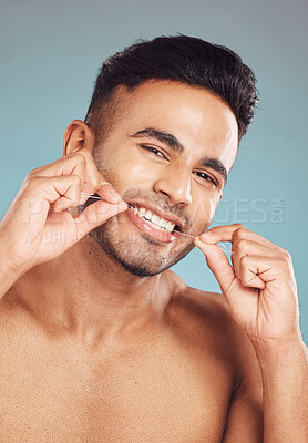 Buy stock photo Portrait of one smiling young indian man flossing his teeth against a blue studio background. Handsome guy grooming and cleaning his mouth for better oral and dental hygiene. Floss daily to prevent tooth decay and gum disease