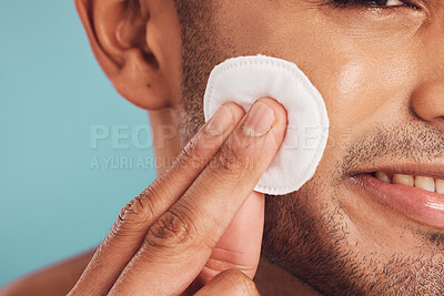 Closeup of one mixed race man wiping a round cotton swab on his face while grooming against a blue studio background. Handsome guy cleaning and exfoliating his face for a healthy complexion and clear skin