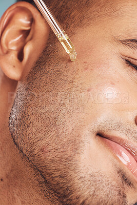 Closeup of one mixed race man using a dropper to apply serum oil to his skin and face against a blue studio background. Guy using a moisturising aftershave product for healthy, smooth and soft skin