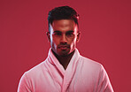 Athletic young male model wearing a bathrobe while posing posing against a red background. Handsome young hispanic man posing in the studio