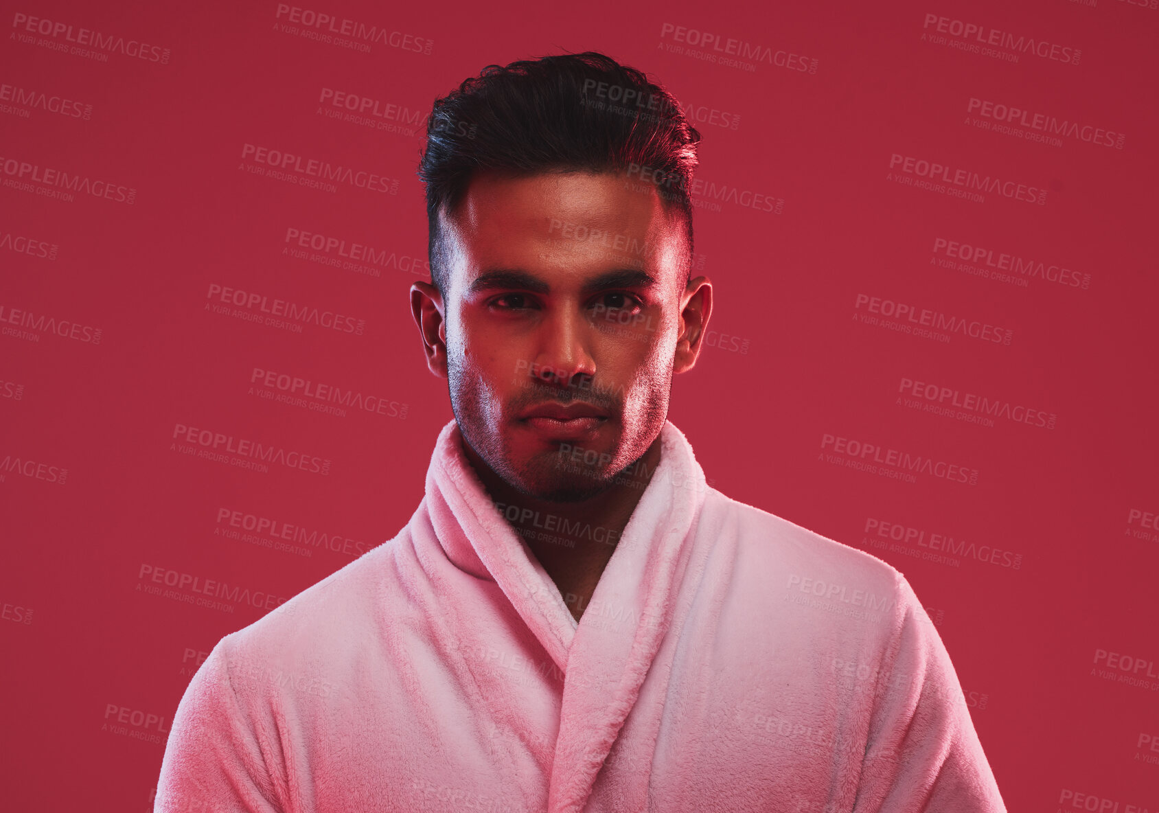 Buy stock photo Athletic young male model wearing a bathrobe while posing posing against a red background. Handsome young hispanic man posing in the studio