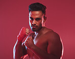 Portrait of one fit and strong handsome mixed race kickboxer isolated against a red studio background and getting ready to fight. Hispanic man posing shirtless in a punching stance. Focused on target
