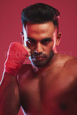 Portrait of one fit and strong handsome mixed race kickboxer isolated against a red studio background and getting ready to fight. Hispanic man posing shirtless in a punching stance. Focused on target