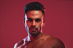 Closeup portrait of bare chested athletic young man posing against a red background. Handsome young masculine hispanic man looking confident while posing in the studio