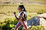 Young african american woman wearing earphones listening to music while running on a mountain trail in the morning. Confident fit black female wearing gymwear jogging alone in nature