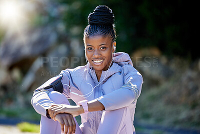 Buy stock photo Fitness, portrait and woman resting after a workout in nature with earphones for music, radio or podcast. Happy, smile and African female athlete sitting after an outdoor cardio running exercise.