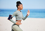 Fit and active African American woman listening to music through earphones and running alone on a beach for workout. Focused black athlete training, exercising and using a cellphone to track progress