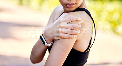 Closeup of one mixed race woman holding her sore shoulder while exercising outdoors. Female athlete suffering with painful arm injury from fractured joint and inflamed muscles during workout. Struggling with stiff body cramps causing discomfort and strain