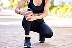 Closeup of one mixed race woman holding her sore knee while exercising outdoors. Female athlete suffering with painful leg injury from fractured joint and inflamed muscles during workout. Struggling with stiff body cramps causing discomfort and strain