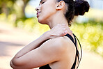 Closeup of one mixed race woman from behind holding neck shoulder while exercising outdoors. Female athlete suffering with painful injury from fractured joint and inflamed muscles during workout. Struggling with stiff body cramps causing discomfort