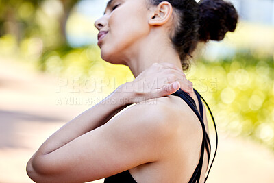 Closeup of one mixed race woman from behind holding neck shoulder while exercising outdoors. Female athlete suffering with painful injury from fractured joint and inflamed muscles during workout. Struggling with stiff body cramps causing discomfort