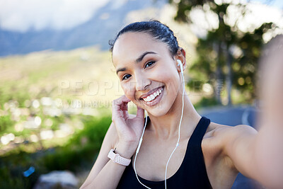 Portrait of one fit young mixed race woman listening to music with earphones and taking selfies on a break from exercise outdoors. Happy female on video call and taking photos for social media during a rest from running workout