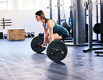 One fit young caucasian man doing deadlifts with a barbell while training in a gym. Focused guy challenging himself by lifting heavy weights to build muscle and endurance during a workout